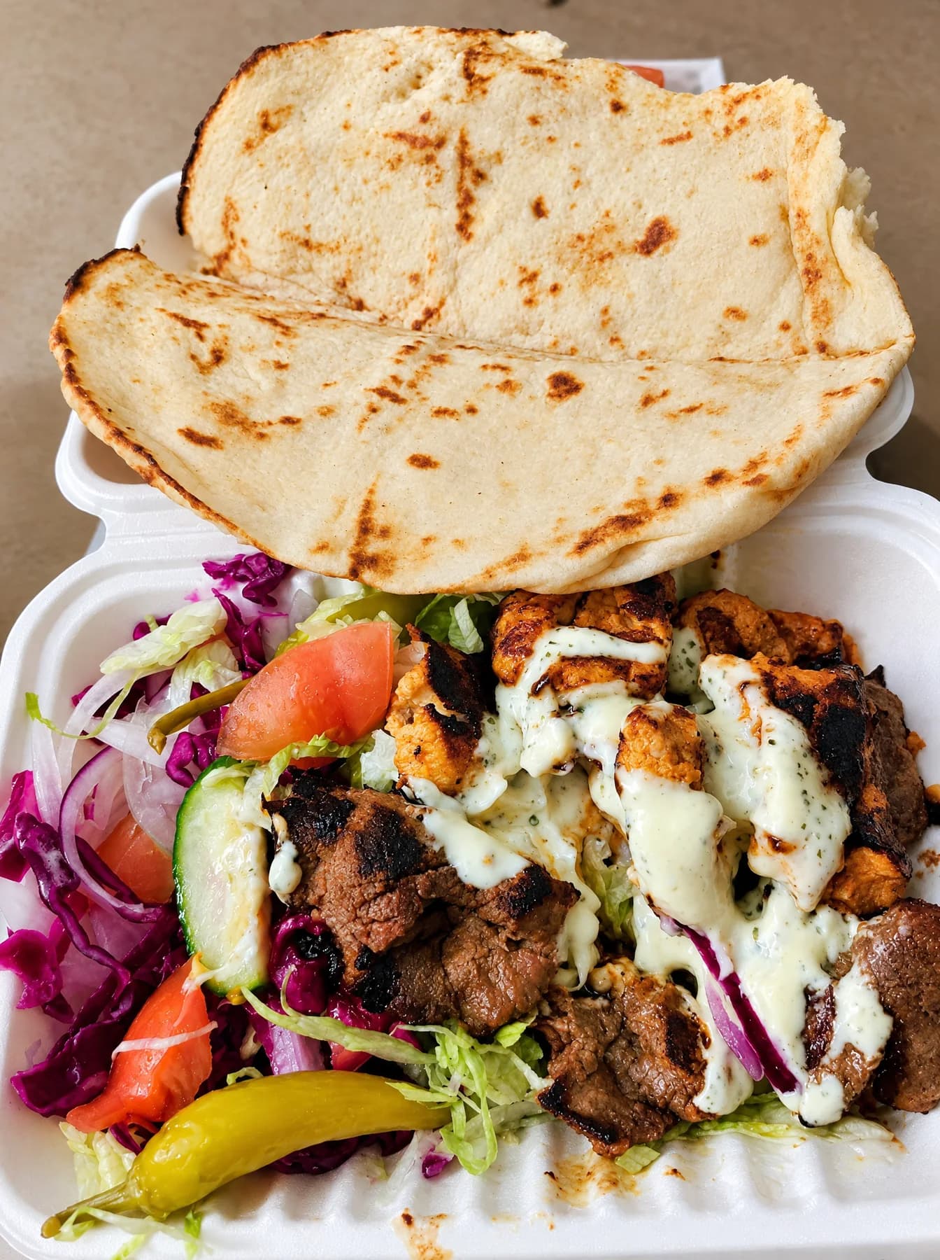 A mixed kebab with salad, garlic sauce and a green chilli, topped with pitta bread