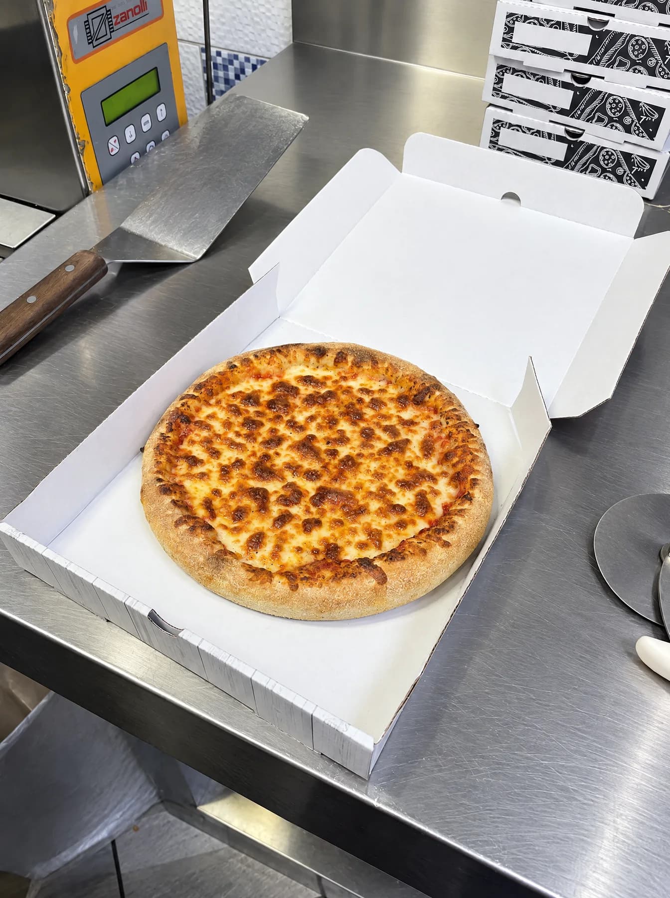 A cheese pizza fresh from the oven in an open box on the steel counter